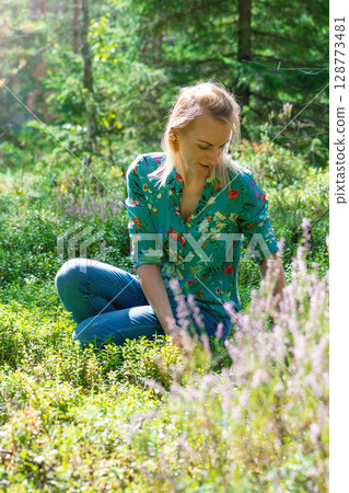 Blonde woman collecting cranberries in forest 128773481