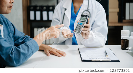Healthcare costs and fees concept.Hand of smart doctor used a calculator and smartphone, tablet for medical costs at hospital 128773801