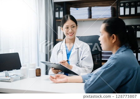 A professional physician talks to discuss results or symptoms and gives a recommendation to a male patient and signs a medical paper at an appointment visit in clinic. 128773807
