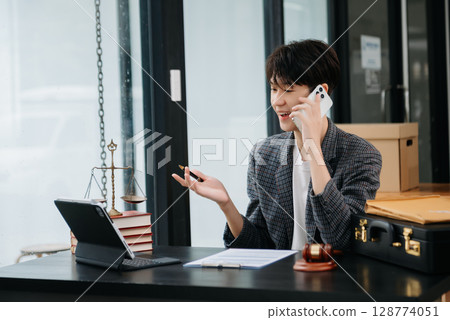 Asian female lawyer chatting online with client on laptop, smartphone discussing details of lawsuit. in modern office Asian female lawyer chatting online with client on laptop, smartphone discussing details of lawsuit. in modern office 128774051