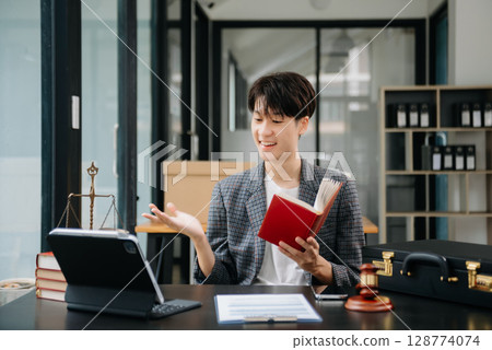 Asian Woman lawyer reading legal book with gavel on table in office. justice and law ,attorney concept. 128774074