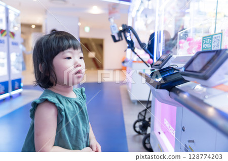 Toddler girl playing with UFO catcher at game center 128774203