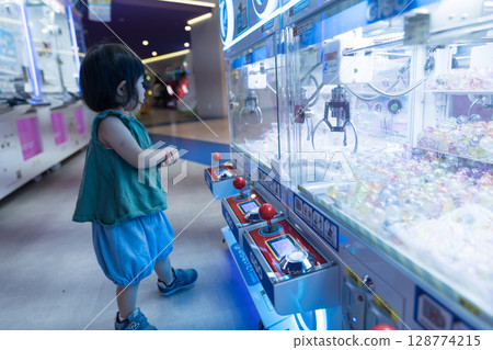 Toddler girl playing with UFO catcher at game center 128774215