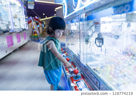 Toddler girl playing with UFO catcher at game center Toddler girl playing with UFO catcher at game center 128774219