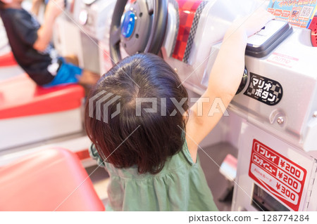 Toddler girl playing racing games at arcade 128774284
