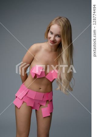 Blonde woman in a studio wearing a creative outfit made of pink sticky notes Blonde woman in a studio wearing a creative outfit made of pink sticky notes 128774494