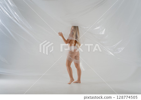 Blonde woman posing in studio with translucent material in creative expression 128774505