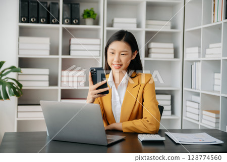 Confident Asian woman with a smile standing holding notepad and tablet at the office. Confident Asian woman with a smile standing holding notepad and tablet at the office. 128774560