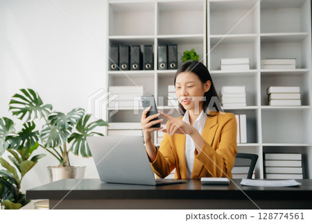 Confident Asian woman with a smile standing holding notepad and tablet at the office. 128774561