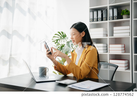 Confident Asian woman with a smile standing holding notepad and tablet at the office. 128774562