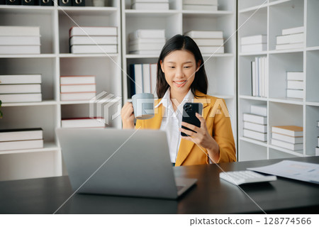 Confident Asian woman with a smile standing holding notepad and tablet at the office. Confident Asian woman with a smile standing holding notepad and tablet at the office. 128774566