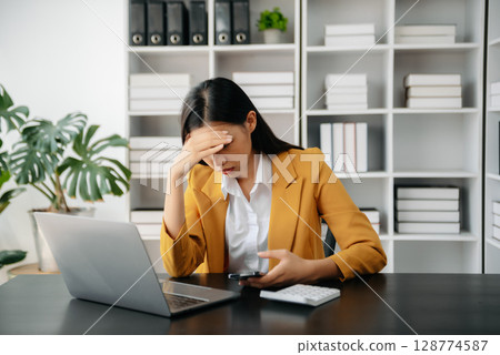 Asian woman feeling migraine head strain.Overworked businesswoman financier while working on laptop and tablet at office. 128774587