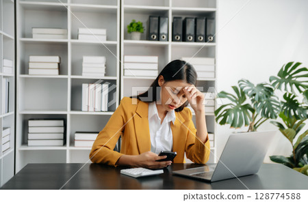 Asian woman feeling migraine head strain.Overworked businesswoman financier while working on laptop and tablet at office. 128774588