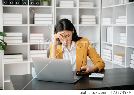 Asian woman feeling migraine head strain.Overworked businesswoman financier while working on laptop and tablet at office. 128774589