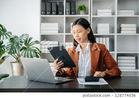 Beautiful Asian business woman typing laptop and tablet Placed at the table at the office Beautiful Asian business woman typing laptop and tablet Placed at the table at the office 128774836