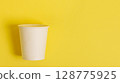 Disposable paper cup for coffee and tea on a bright orange background. 128775925