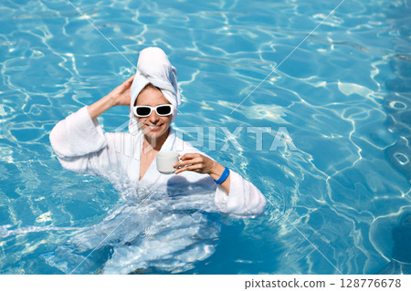 A girl in a white coat swims in a blue pool. Wearing sunglasses and a towel. Epilation of legs, varicose veins. Rest, relaxation on the beach, at the hotel. A woman in freedom. Vacation. High quality A girl in a white coat swims in a blue pool. Wearing sunglasses and a towel. Epilation of legs, varicose veins. Rest, relaxation on the beach, at the hotel. A woman in freedom. Vacation. High quality 128776678