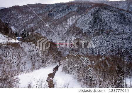 The red Takai Bridge stands out against the snowy scenery and the winter valley around Yamada Onsen (Nagano Prefecture) 128777024