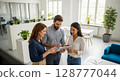 Three business colleagues collaborating around a tablet in a modern office space. 128777044