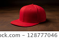 A vibrant red flat-brim baseball cap rests on a dark wooden surface. 128777046