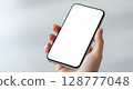 A hand holding a modern smartphone with a blank white screen, ready for use. 128777048
