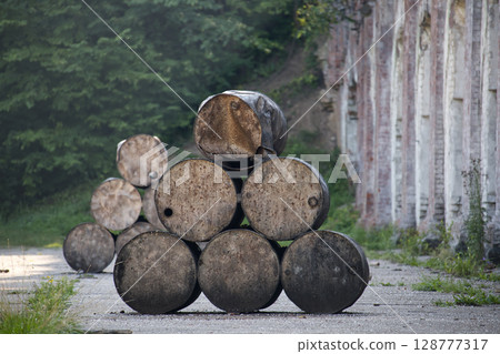 Stack of Weathered Metal Barrels Outdoors Near an Abandoned Wall in a Forest Stack of Weathered Metal Barrels Outdoors Near an Abandoned Wall in a Forest 128777317
