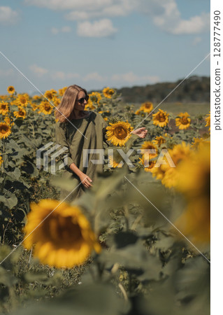 A girl in a pink skirt and a white T-shirt walks through a field of blooming yellow sunflowers. A woman dances, rejoices, smiles, enjoys life, warmth, summer, the sun. High quality FullHD footage 128777490