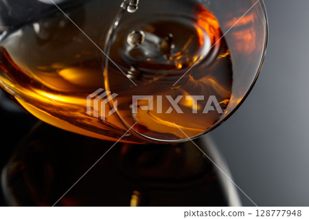 Glass of brandy on a black reflective background. 128777948