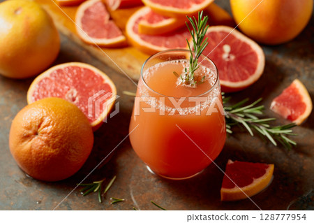 A glass of grapefruit juice garnished with a rosemary sprig. 128777954