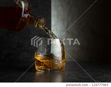 Pouring whiskey from a bottle into a glass. Pouring whiskey from a bottle into a glass. 128777965