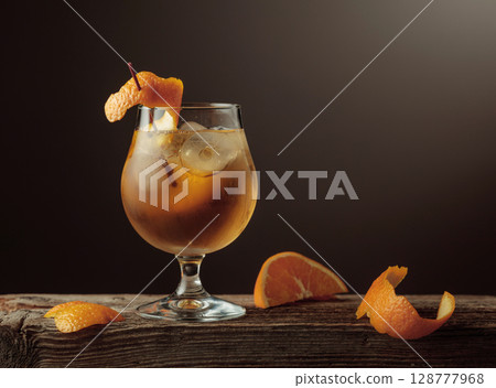 Old Fashioned cocktail with a ice, garnished with an orange peel on a old wooden board. Old Fashioned cocktail with a ice, garnished with an orange peel on a old wooden board. 128777968