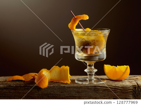 Old Fashioned cocktail with a ice, garnished with an orange peel on a old wooden board. 128777969