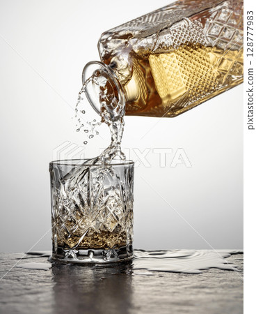 Whiskey is poured from a decanter into a crystal glass. 128777983
