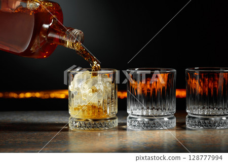 Whiskey is poured into a glass with ice. 128777994