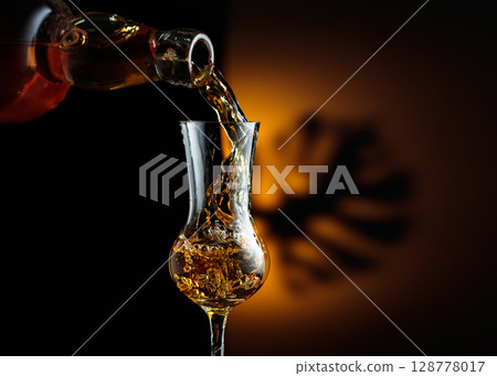 Rum being poured from a bottle into a glass. 128778017