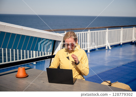 Woman working on laptop outdoors on ferry deck on sunny windy day 128779302