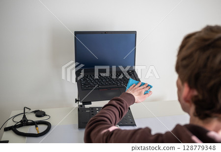 Person cleaning laptop screen with microfiber cloth on adjustable desk stand in home office Person cleaning laptop screen with microfiber cloth on adjustable desk stand in home office 128779348
