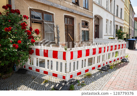 old building under renovation with red and white construction barriers and boarded window in Germany 128779376