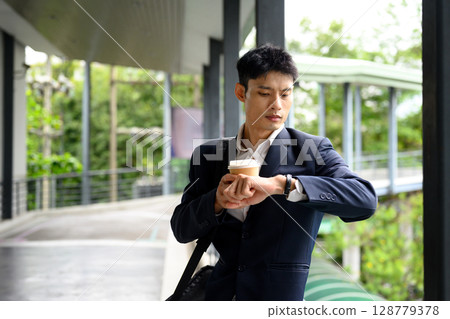 Businessman rushing to meeting, holding takeaway coffee and checking the time 128779378
