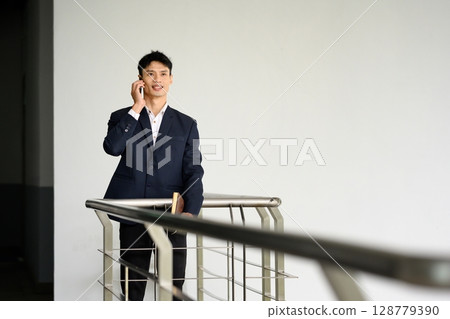 Confident businessman talking on smartphone while standing by modern railing 128779390