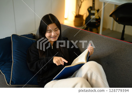 Relaxed teenager lounging on a sofa and reading a book on couch 128779394