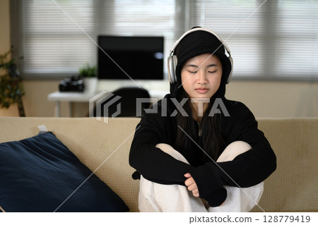 Sad teenage girl at home, listening to music with a serious expression. Mental health concept 128779419