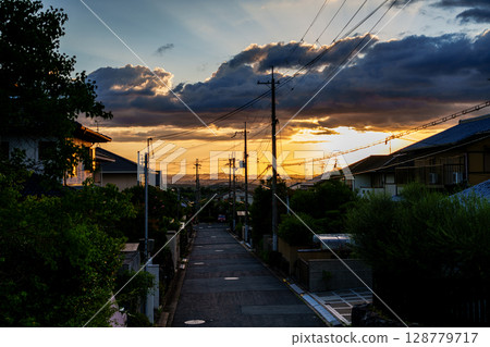 夕陽西下，奈良市的山腰天空被染成了金色。城市道路兩旁的電線桿和夕陽的天空交相輝映。 128779717