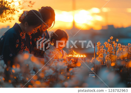 a family in traditional Japanese attire visiting a cemetery during Obon, lighting incense and placing flowers on a gravestone 128782963