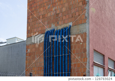 Blue electrical conduits securely run along weathered brick building wall, illustrating vital urban utility infrastructure and modern construction development Blue electrical conduits securely run along weathered brick building wall, illustrating vital urban utility infrastructure and modern construction development 128783024