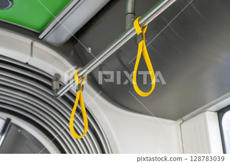 Modern public transit interior showcases a shining chrome handrail with vibrant yellow hanging handles, essential for passenger safety and urban convenience 128783039