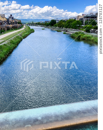 A white egret flying over the water of the Kamo River in Kyoto, Japan on a summer day, blue sky and white clouds, seen from Shijo Ohashi Bridge A white egret flying over the water of the Kamo River in Kyoto, Japan on a summer day, blue sky and white clouds, seen from Shijo Ohashi Bridge 128783127