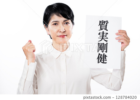 A senior woman showing her motivation with a fist pump while holding a piece of paper with the words "Simple and strong" written on it 128784020