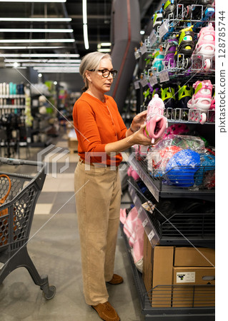 Mature woman shopping in a large home improvement store examining product quality and selection 128785744