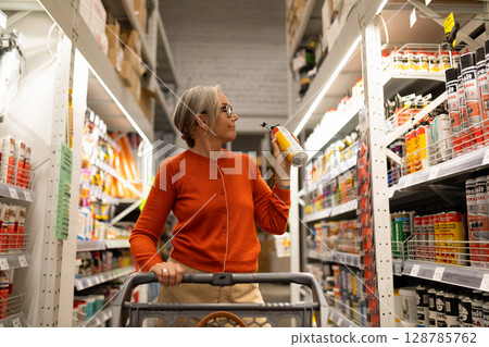 Middle-aged woman shopping in a modern construction hypermarket, exploring diverse product sections 128785762
